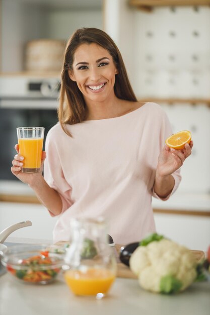 Foto de una mujer joven bebiendo jugo de naranja fresco en su cocina.