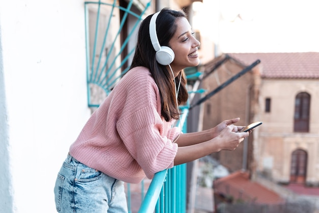 Foto de mujer joven y bonita escuchando música con el teléfono inteligente mientras está de pie en la azotea de su casa.