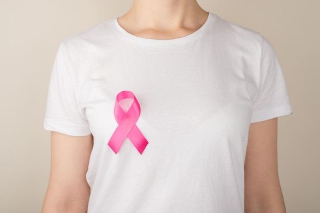 Foto de mujer joven en camiseta blanca con símbolo de cinta rosa de concienciación sobre el cáncer de mama sobre fondo gris aislado