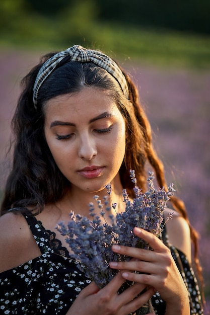 Foto de mujer joven caucásica en vestido sosteniendo ramo de flores, al aire libre a través del campo de lavanda en verano