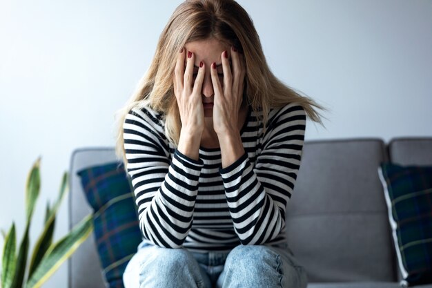 Foto foto de mujer joven deprimida pensando en sus problemas mientras está sentado en el sofá de casa.