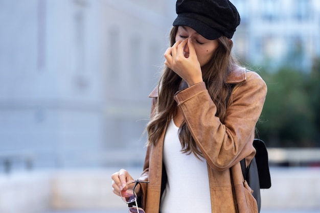 Foto de mujer joven dolorosa que sufre dolor de cabeza mientras está de pie en la calle.