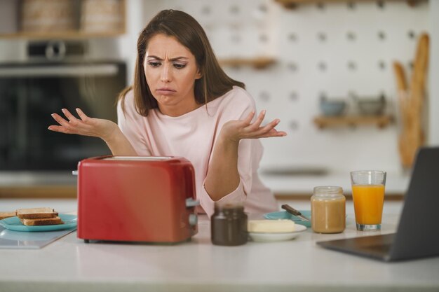 Foto de una mujer joven esperando una tostada en una tostadora para desayunar en casa.