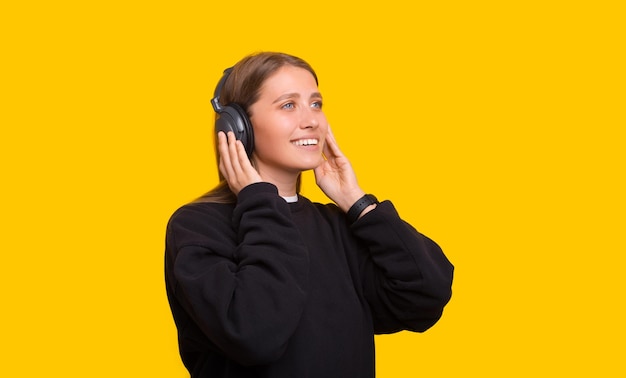 Foto de mujer joven feliz ajustando los auriculares mientras escucha música aislado sobre fondo amarillo