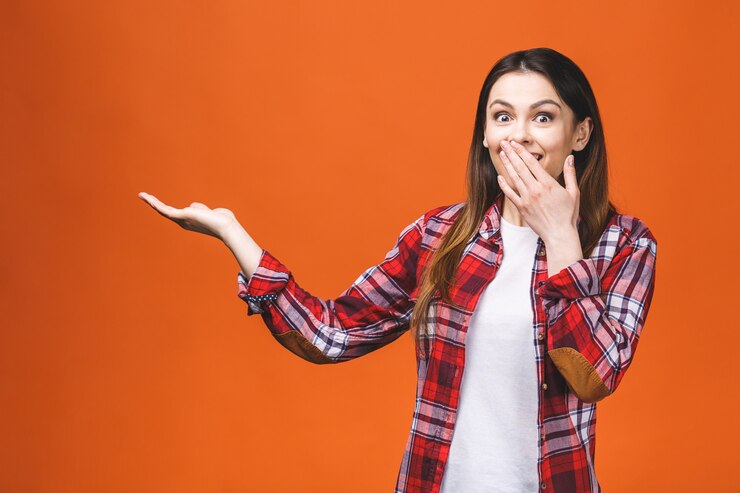 Foto foto de la mujer joven feliz que se coloca aislada sobre fondo anaranjado de la pared. mirando la cámara mostrando copyspace apuntando.
