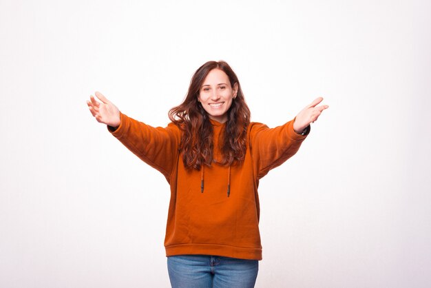Foto de mujer joven haciendo gesto de bienvenida y sonriendo sobre la pared blanca