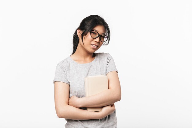 Foto de la mujer joven hermosa feliz asiática que presenta aislada sobre la pared blanca que sostiene la lectura del libro.