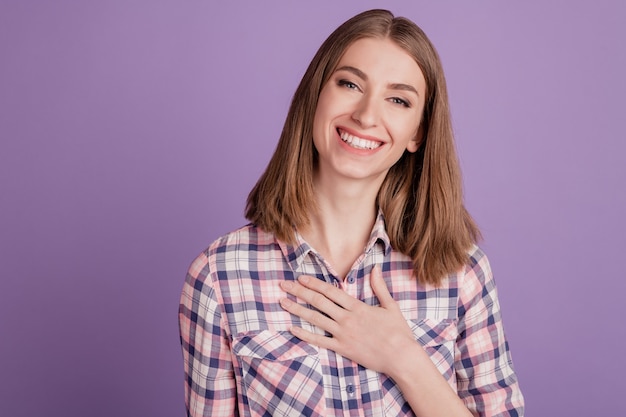 Foto de mujer joven con la mano en el pecho demuestra signo de gratitud y afecto sonrisa sincera aislado sobre fondo violeta