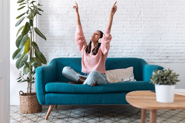 Foto de mujer joven motivada escuchando música con tableta digital mientras está sentado en el sofá en casa.