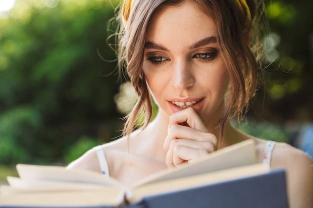 Foto de mujer joven muy hermosa asombrosa seria en el libro de lectura del parque verde.