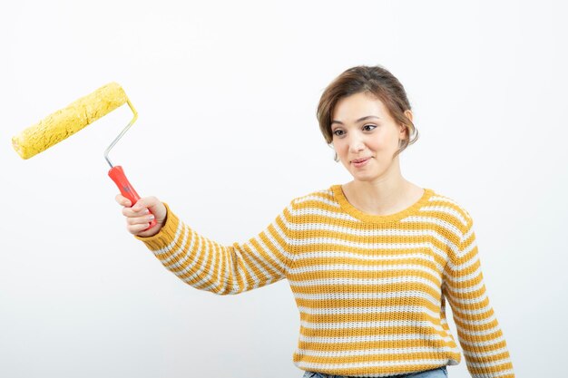 Foto de mujer joven de pie y sosteniendo un rodillo de pintura en la mano. foto de alta calidad