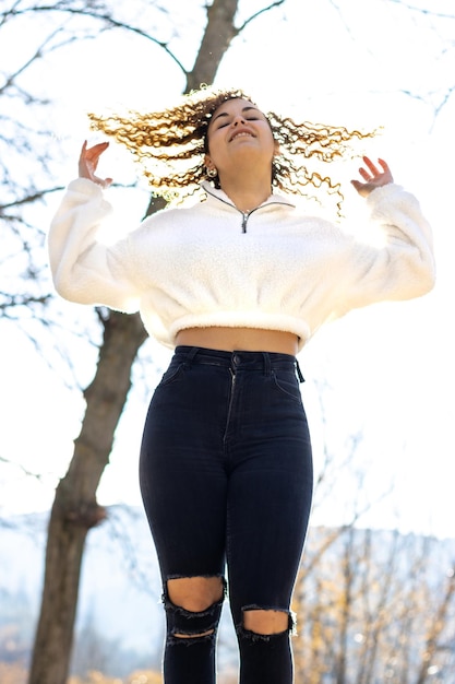 Foto de una mujer joven posando frente a un árbol usando jeans desgastados