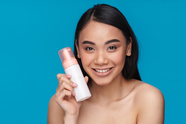 Foto de mujer joven positiva asiática posando aislada en la pared azul con espuma limpiadora de mousse.