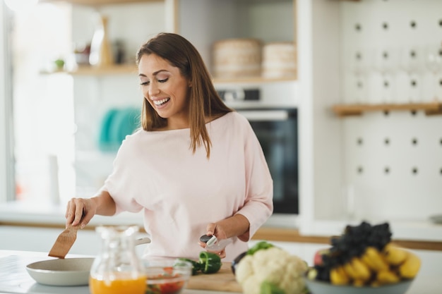 Foto de una mujer joven que prepara una comida saludable en la estufa de su cocina.