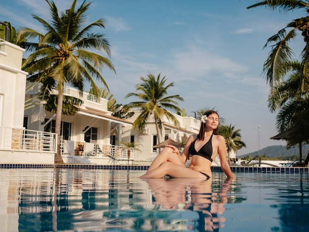 Foto de una mujer joven relajándose junto a la piscina de lujo Vacaciones de verano Mujer feliz disfrutando de un día soleado de verano junto a la piscina