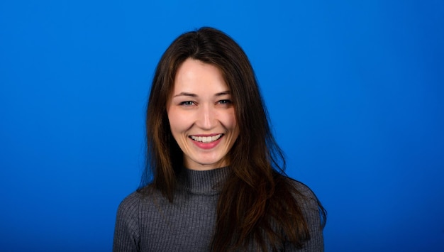 Foto de mujer joven sonriente y alegre en vestido gris sobre fondo azul. Retrato emocional