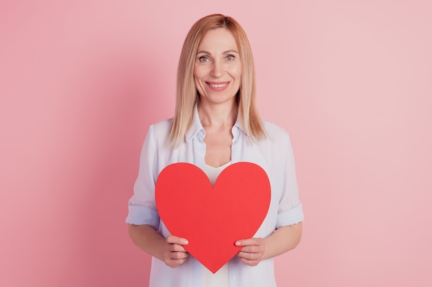 Foto de mujer joven sosteniendo en la mano gran corazón grande día de San Valentín amor romance aislado sobre fondo de color rosa