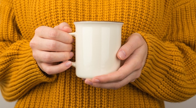 Foto de mujer joven en suéter amarillo acogedor sosteniendo taza blanca de bebida caliente con espacio vacío