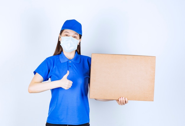 Foto de mujer joven en uniforme con caja de papel mostrando el pulgar hacia arriba.