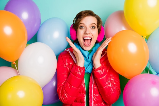 Foto de mujer loca rodeada de muchos globos de aire de colores sorpresa fiesta de cumpleaños alégrate usar abrigo rojo casual bufanda puente rosa orejeras aislado pared de color verde azulado