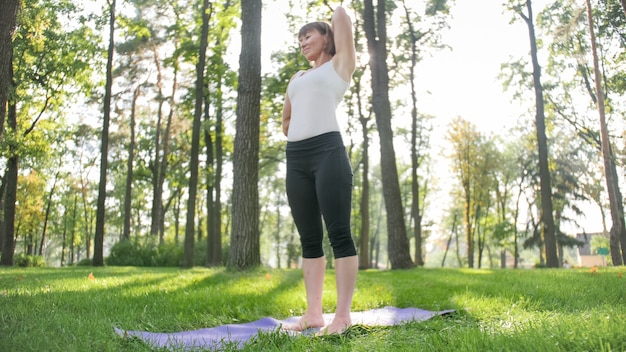 Foto de mujer de mediana edad en ropa de sportrs practicando yoga al aire libre en el parque. Mujer de mediana edad estirando y meditando en el bosque