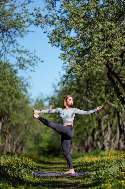 Foto foto de mujer mirando al lado de estar de pie sobre una pierna practicando yoga en el bosque durante el día