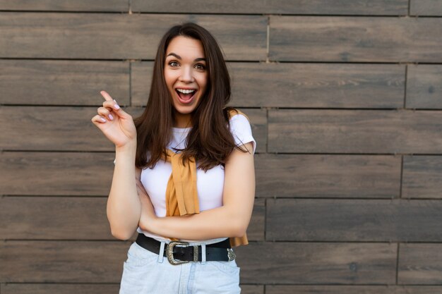 Foto de mujer morena bastante joven alegre feliz positiva emocional en traje de moda. Hermosa persona femenina atractiva de pie afuera en la calle y mostrando emociones sinceras.