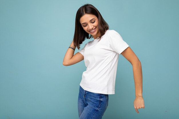 Foto foto de mujer morena hermosa joven alegre sonriente positiva con emociones sinceras vistiendo camiseta blanca casual para maqueta aislada sobre fondo azul con espacio vacío y baile.