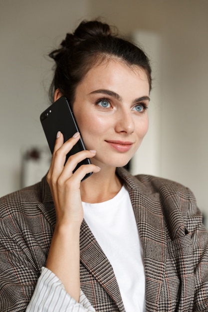 Foto de una mujer de negocios bastante joven adentro en casa hablando por teléfono móvil.