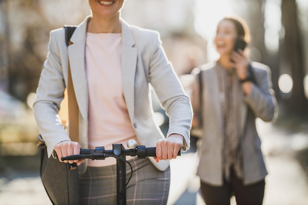 Foto foto de una mujer de negocios irreconocible montando un scooter eléctrico de camino al trabajo.
