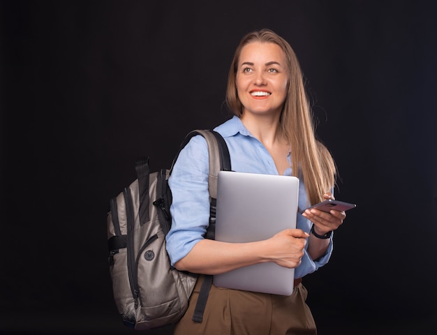 Foto de mujer de negocios joven con mochila y con smartphone sobre fondo oscuro