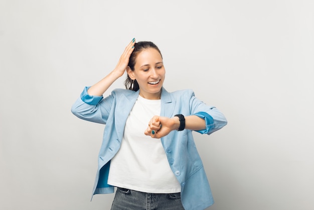Foto de mujer de negocios joven en pie casual sobre fondo blanco y mirando asombrado por smartwatch