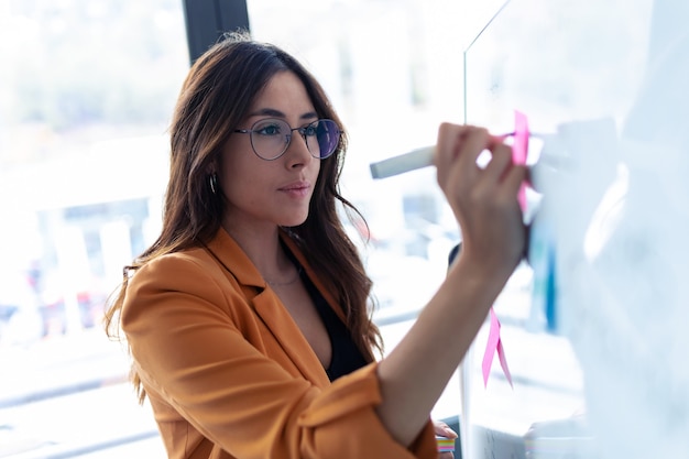 Foto foto de mujer de negocios joven que trabaja en la pizarra con pegatinas de post-it en la oficina.