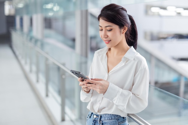 Foto mujer de negocios mirando teléfono inteligente Oficina loft de espacio abierto Fondo de ventanas panorámicas