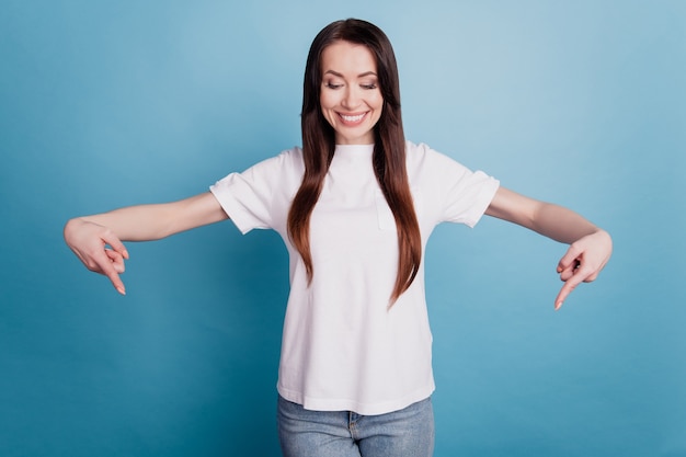 Foto de mujer positiva señalar con el dedo hacia abajo aislado sobre fondo azul.