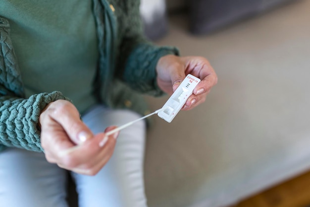 Foto de una mujer que usa un hisopo de algodón mientras realiza una prueba de PCR de coronavirus. Mujer toma muestra de coronavirus de su nariz en casa. Mujer mayor en casa usando un hisopo nasal para COVID-19.