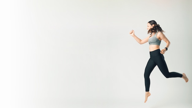 Foto de mujer en ropa deportiva saltando sobre fondo blanco con copyspace