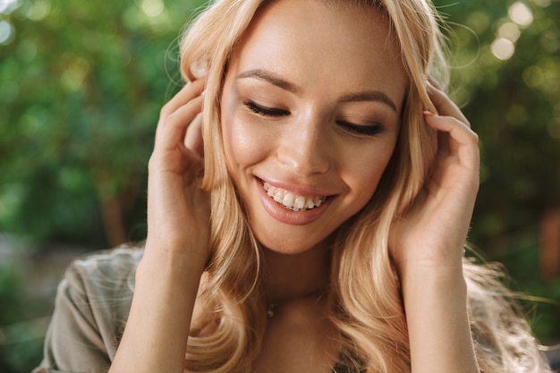 Foto de mujer rubia sensual sonriente en vestido tocando el pelo