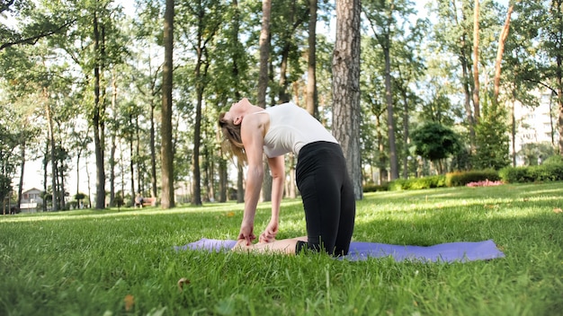 Foto de mujer sonriente de mediana edad practicando yoga y meditando en el parque. Mujer estirando y haciendo fitness en mat en el bosque