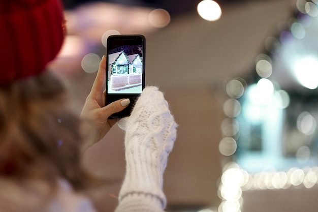 Foto foto de mujer tomando smartphone con guirnaldas y luces navideñas en la festiva feria de navidad o año nuevo.