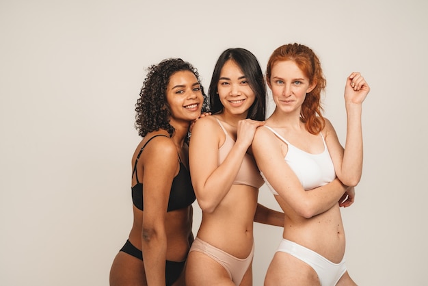 Foto de mujeres lindas optimistas, amigas multirraciales, usan ropa interior. Las mujeres feministas sonríen y se ven felices.