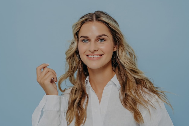 Foto na cabeça de uma linda mulher branca, sorrindo amplamente para a câmera, demonstrando seus dentes brancos, mulher feliz com cabelo perfeitamente estilizado e pele radiante e saudável isolada contra o fundo azul do estúdio