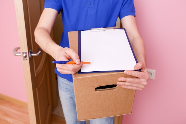 Foto Nahaufnahme des Kuriers mit Stift, leerem Blatt Papier, Pappkarton in der Wohnung