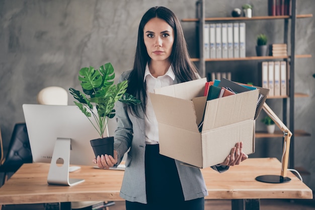 Foto de la niña abogada del director ejecutivo serio tiene crisis de la empresa en quiebra mantener pertenencias caja de cartón con planta de flores dejar de ocupar usar traje de chaqueta de chaqueta en el lugar de trabajo de la estación de trabajo