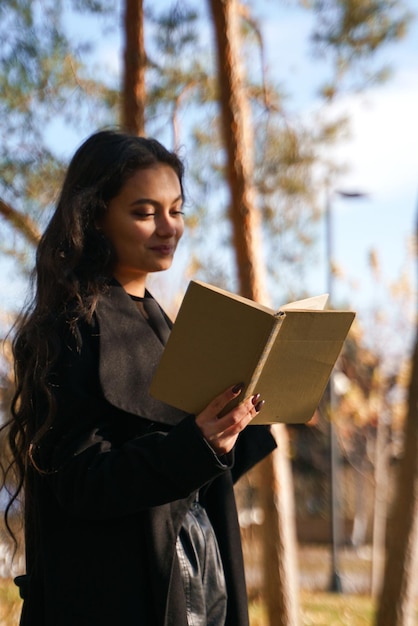 Foto foto de una niña con un abrigo negro que está en el parque y lee un libro