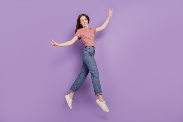 Foto de niña alegre saltando en el aire aislado sobre fondo violeta