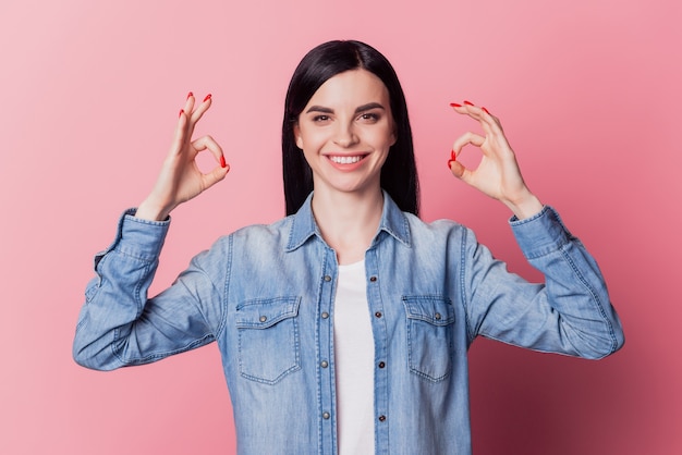 Foto de niña bonita alegre que muestra bien firmar bien trato fresco de pie satisfecho contra el fondo de color rosa