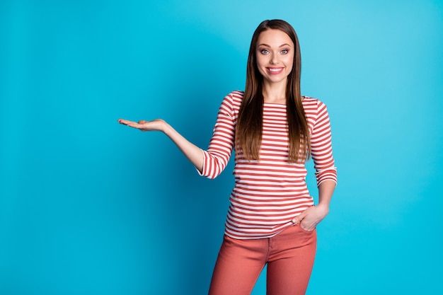 Foto de niña emocionada positiva promotora sostenga la mano presentar anuncios promo recomendar sugerir seleccionar ropa lucir bien aislado sobre fondo de color azul