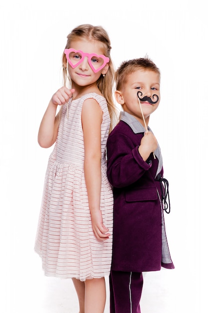 Foto de niña con unas gafas de cartón en forma de corazón y un niño con un bigote de cartón posando