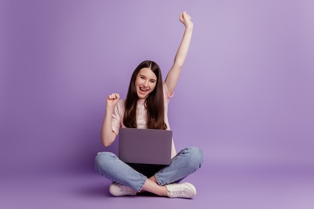 Foto de niña con laptop levantar las manos celebran la victoria sobre fondo púrpura